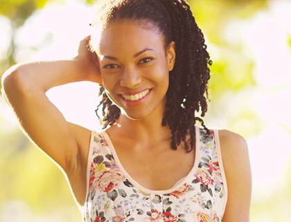 Outdoor photo of an African American woman with braids smiling; for information on smile creation from Bayou Dental Group in Monroe, LA.