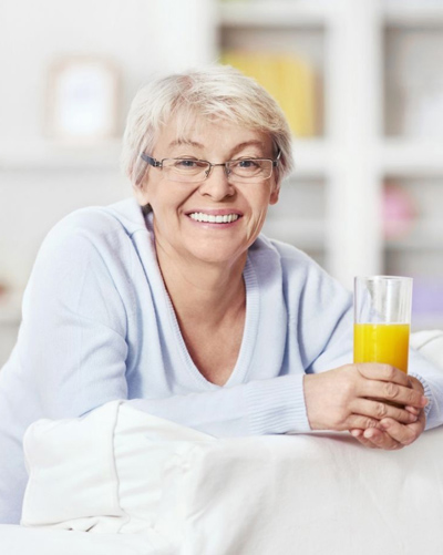Senior woman smiling and holding a glass of orange juice - for natural-looking dentures info from Bayou Dental Group