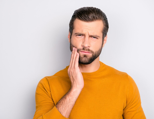 Brunetee man with beard holding the right side of his face - for information on sedation and impacted wisdom teeth from Monroe, LA dentist David Finley
