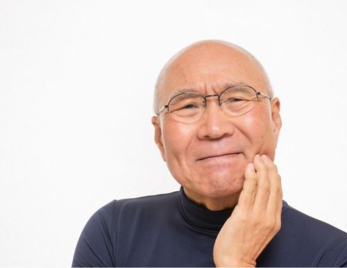 Senior Asian man holding the side of his face portraying jaw swelling and pain after extractions for dentures